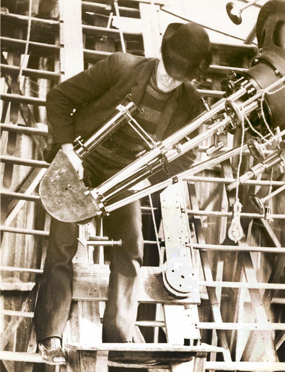 Slipher stands with the Brashear spectrograph, mounted on the 24-inch Clark Telescope, with which he made his many spectroscopic discoveries — including his observations of multiple spiral nebulae, most of which were rushing away from Earth at great speed, signaling the expansion of the universe.